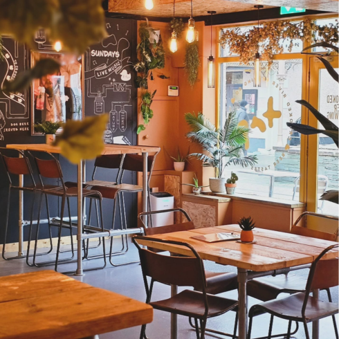 Inside the Crooked River Tap bar in Keswick - wooden tables and high stools, hanging plants and the street outside the window