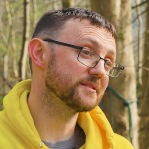 Headshot of a man in a yellow hoodie with glasses