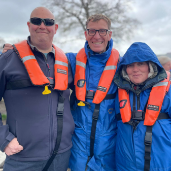 Two men and a woman in waterproofs and buoyancy aids smiling
