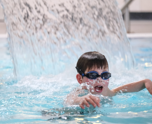 Boy in goggles under swimming pool fountain