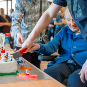 Old man in wheelchair cutting a birthday cake with help