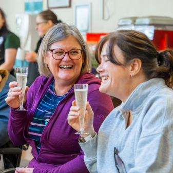 Two women in wheelchairs enjoying a glass of fizz laughing at Calvert Lakes