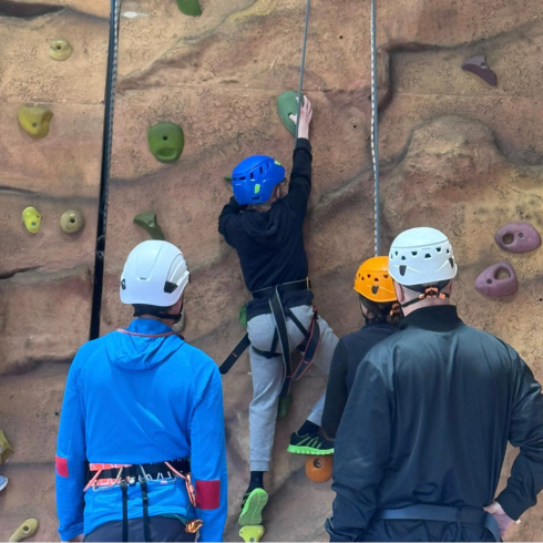 Young man on climbing wall with two instructors watching