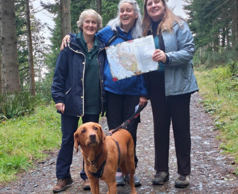 three women and a dog holding a map in the woods