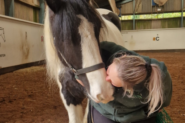 Stables volunteer nuzzling a brown and white horse in a stables arena