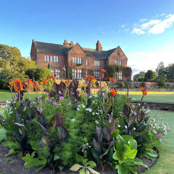 Flowering plants in the foreground with sandstone country home Nunwick Hall behind