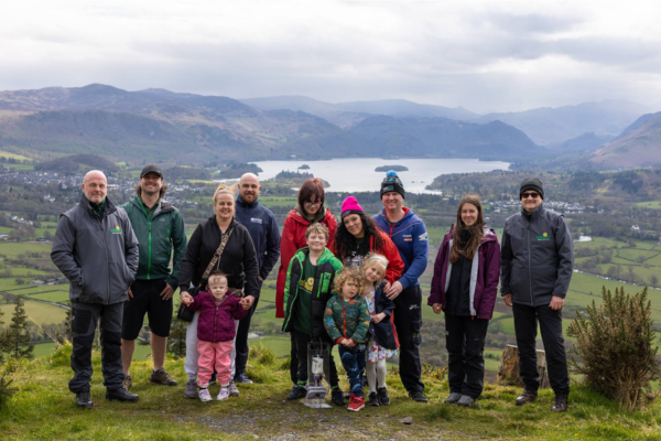 Group of adults and children standing on a mountain with views of a lake and countryside behind them