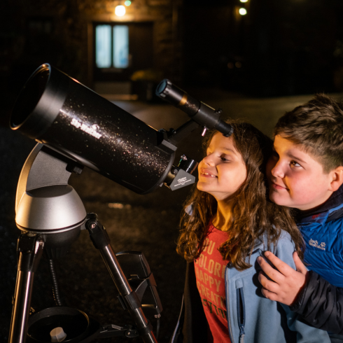 Brother and sister looking through large telescope at night