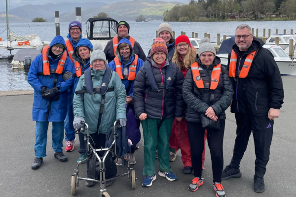 Group of adults in front of a lake wearing buoyancy aids ready for sailing session