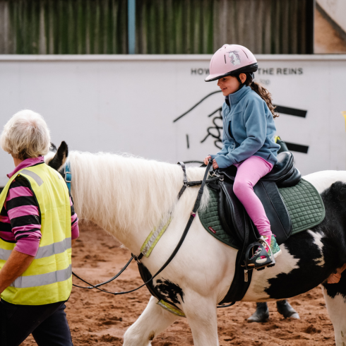 Young girl riding a horse being supported by a stables volunteer