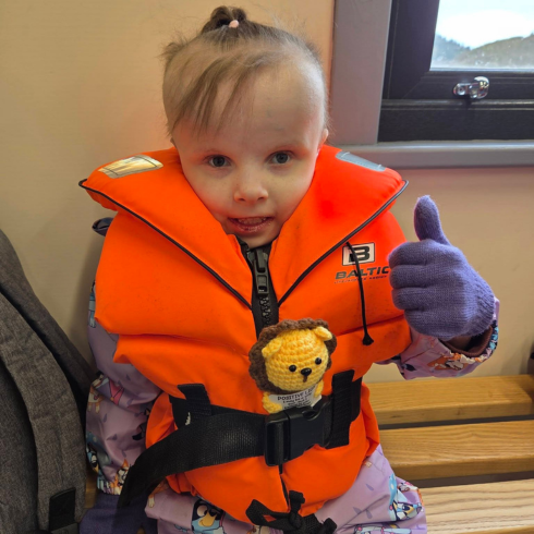 Young girl in orange buoyancy aid with her thumb up in the boathouse before canoing