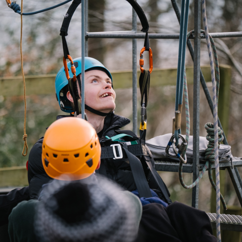 Boy in helmet smiling as he looks up at a ladder ready to strap into a zip wire