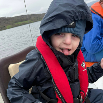 Young boy with waterproofs and buoyancy aid sticking his tongue out on a catamaran