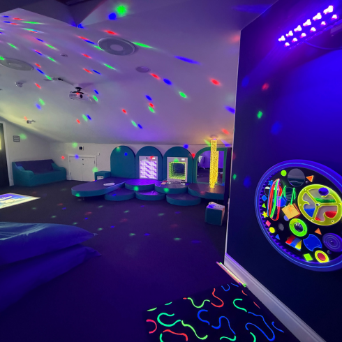 Sensory room showing UV wall, interactive floor projectors, coloured spotlights and padded cushions