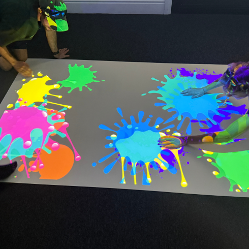 Interactive floor projector with people trying to pop paint balloons on the floor