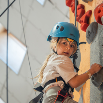 Small girl with a blue helmet on an indoor climbing wall