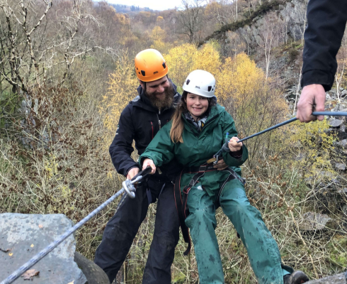 Young girl being supported while abseiling down a rock wall with an instructor