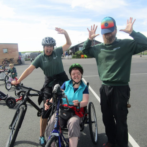 Woman on a bike in between two instructors, one on a bike and another with a cap over his face