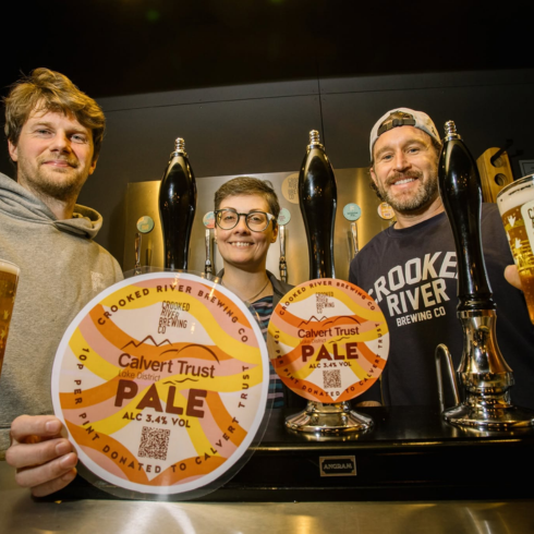 Three people behind a bar with Calvert Pale Ale on tap and a pint of ales
