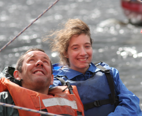 Two people smiling with wind in their hair as they sail on Bassenthwaite Lake