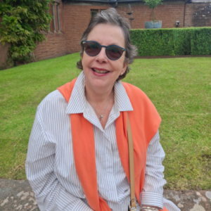 Carol Moreton at Nunwick Hall sitting on a wall with lawn and garden behind